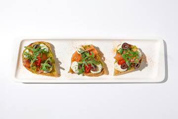 Aesthetic composition with salmon bruschetta on white backgroundover white wall. Italian bruschetta with salmon, avocado, cheese and olives on fine dining in summer. Elegant menu concept.