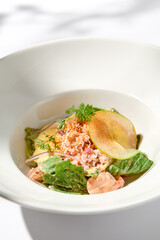 Elegant salad with crab meat, espuma sauce and lettuce on white table with harsh shadows. Green salad with crab and creamy sauce in summer menu. Aesthetic food. Seafood appetizer.
