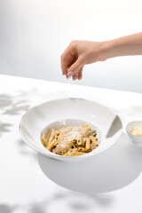 Woman hand sprinkle cheese on italian pasta in white plate. Preparation food. Female hand cooks pasta penne with cheese. Trendy menu concept with hands.