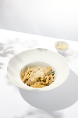 Italian pasta penne with chicken and mushrooms in creamy sauce. Mushroom and chicken pasta on white plate with shadows of sunlight. Summer italian lunch Penne with mushroom sauce on light background