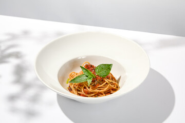 Vegetarian pasta with basil and tomatoes on white plate. Tomato pasta in summer menu with hard shadows Spaghetti with tomatoes on light background. Vegan food - spaghetti marinara