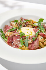 Homemade pasta with pastrami and creamy sauce with cheese. Italian pasta pappardelle with beef and sauce on white table Italian food in summer dining with shadows of sunlight