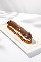Chocolate eclair on white plate. French dessert stuffed custard cream. Eclair with coffee flavours Chocolate dessert on restaurant plate. Cchocolate eclair on light background