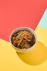 Asian fried buckwheat noodles with chicken on coloured background Fried noodles in ceramic bowl on yellow, red and blue background. Stir-fry soba in trendy style with shadows. Vibrant food
