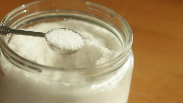 A teaspoon of table sea salt is being scooped with stainless steel measuring spoon cup