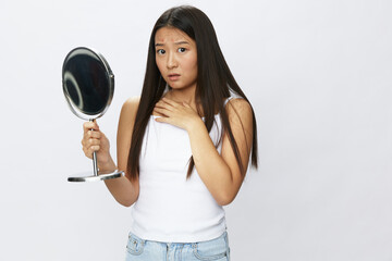 Asian woman with mirror in hand facial skin problems, acne and inflammation, red rash and...