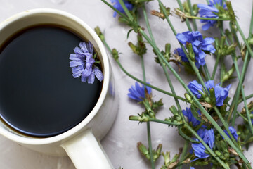 chicory drink and floating chicory flower in a coffee mug next to chicory flowers