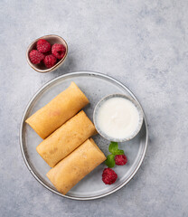 Homemade crepes with raspberry and sour cream on a plate on a light background.