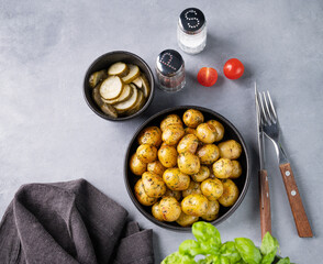 Young roasted baby potatoes in a black  pan with tomatoes and cucumber on a blue background