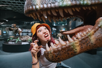 girl visitor to the dinosaur exhibition is fooling around and trying to scare the raptor