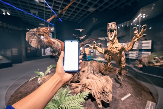 26 July 2022, Munster Natural History Museum, Germany: Visitor hand with blank smartphone screen at the Exhibition of terrifying feathered dinosaur deinonychus