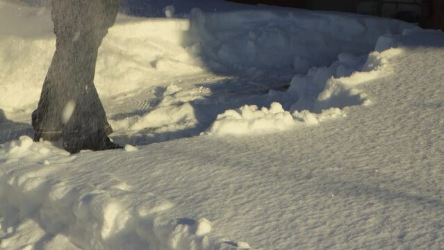Close-up of a man clearing a large white snowdrift with a shovel. Large snowdrifts around after a snowstorm, sunny day. City life, heavy snowfall. UHD 4K.