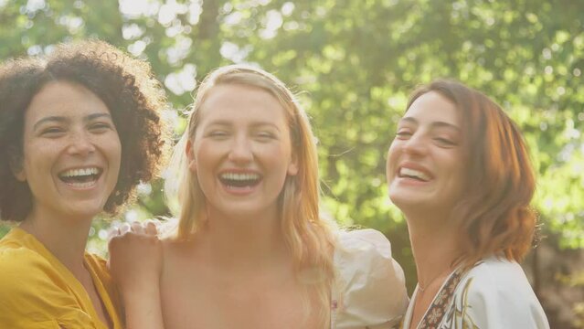 Portrait of three female friends sitting outdoors in summer garden at home relaxing and talking together - shot in slow motion 