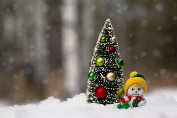 Miniature figurines of Christmas tree and a snowman in the snowy forest.