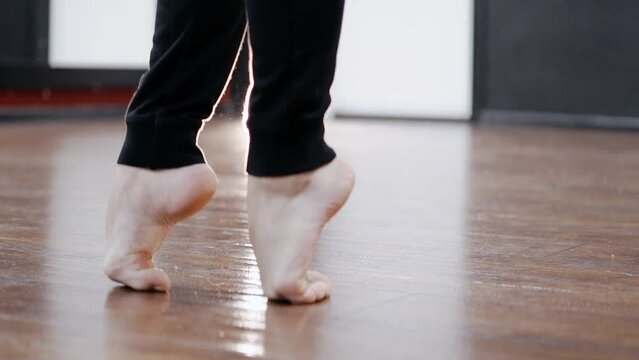 Barefoot man practicing ballet and standing on his toes at a studio, feet close up of Caucasian dancer