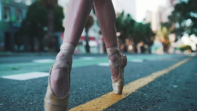 Ballet ballerina walking outdoor on the street on the tip of her toes, low angle close up of feet using ballet slippers