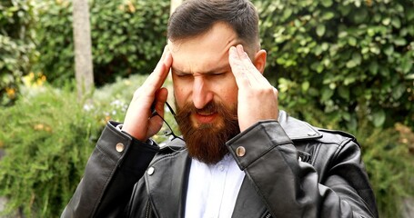 Tired and sad bearded man has a severe headache, a businessman outside the office, holding hands behind his head.