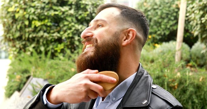 Young bearded man brushing his beard outdoor.