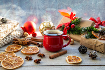 Christmas mood, holiday atmosphere. Red cup of coffee, Christmas gift boxes, Christmas tree golden ball, cones, star anise, cinnamon on a wooden windowsill.