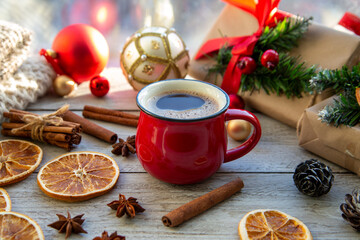 Christmas mood, holiday atmosphere. Red cup of coffee, Christmas gift boxes, Christmas tree golden ball, cones, star anise, cinnamon on a wooden windowsill.