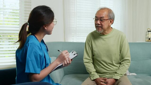 Elderly man takes doctor at home telling about health complaints, Asian young nurse writing prescription clipboard while talking during home visit sick senior old man, Healthcare and medical concept