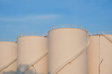 Morning sunlight on surface of white storage fuel tanks group against blue sky in petroleum industrial area 