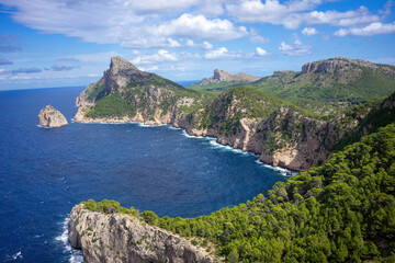 Landscape shot of the wild coastal landscape of Cap Formentor in Mallorca Spain. Cliffs in the sea on a sunny day with blue sky and clouds. Green landscape with a lot of forest from above.