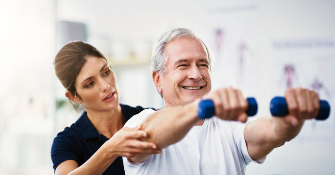 Physiotherapy, senior man and dumbbell exercise, injury rehabilitation or workout at health clinic. Happy elderly patient, woman physiotherapist or muscle training for strong body, care or fitness