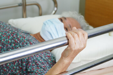 Asian elder senior woman patient holding bed rail while lie down with hope waiting her family in hospital.