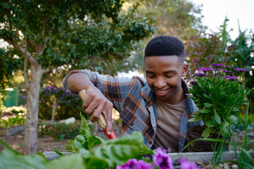 Young black man in checked shirt smiling while using spade in flowerbed in garden center