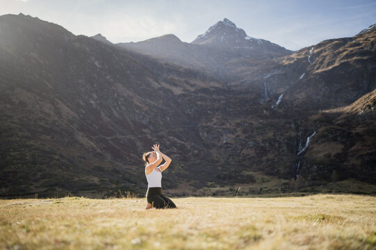 Woman kneeling in an alpine meadow with her hands in prayer pose on her forehead, Gastein, Austria