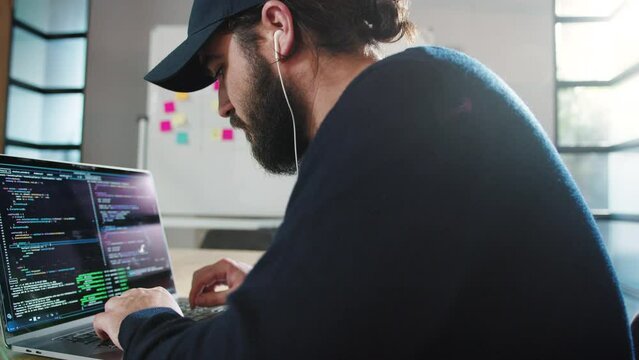 Programmer creating a computer code in an office. Male software developer sitting and working on a laptop. Young business man working in a tech company.