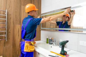 The worker installs the mirror in the bathroom