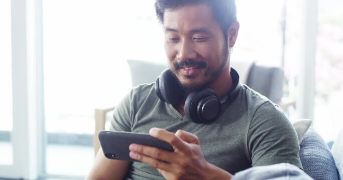Asian man, gamer and relax with phone on sofa playing video games, streaming movies or entertainment at home. Man smiling relaxing on living room couch enjoying wireless mobile gaming on smartphone