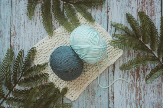 Overhead view of two balls of wool on crochet squares on a table with fir branches