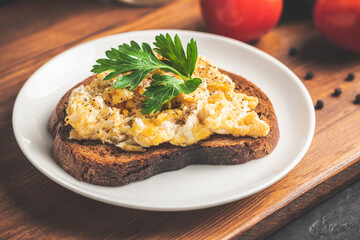 Scrambled eggs with parsley on bread at white plate, homemade healthy breakfast on wooden board