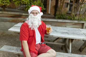 A Santa Claus at Christmas time in  the Australian summer holding a beer