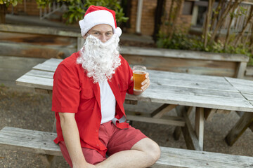 A Santa Claus at Christmas time in  the Australian summer holding a beer