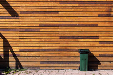 Green trash bin stands near wooden wall