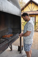 A man fries pork skewers on a metal grill. Rest at the recreation center. The process of cooking fried meat on coals. The guy stands near the barbecue with meat on skewers is warm from the coals.