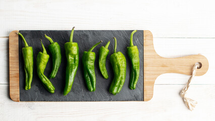 Green peppers on slate plate on white wooden background