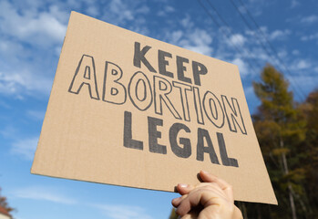 Female hand holding sign with slogan Keep Abortion Legal. Woman with placard supporting abortion...