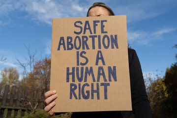Woman holding sign with slogan Safe abortion is a human right. Female protester with placard...