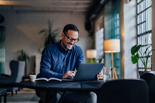 Smiling adult man typing something over the laptop, working online.