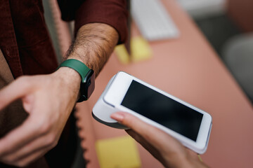 Businessman paying with a smart watch, putting it close to the paying machine.