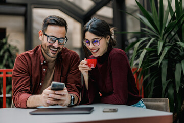 Smiling female holding a cup of coffee while a businessman showing her something over the mobile phone.