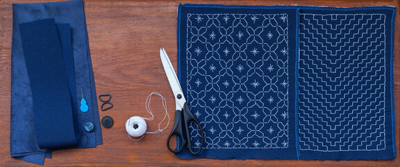 Hand embroidery in Sashiko style with white threads of geometric pattern on blue fabric and sewing...