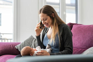 Young mother on the sofa talking on the phone with a baby in tow