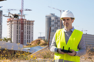 Man launches a quadcopter. An engineer flies a drone next to a construction site. Concept - construction observation with a drone.  Construction cranes on sunset sky