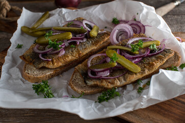 Fried herring with red onions, pickles on buttered and toasted rye bread on wooden table